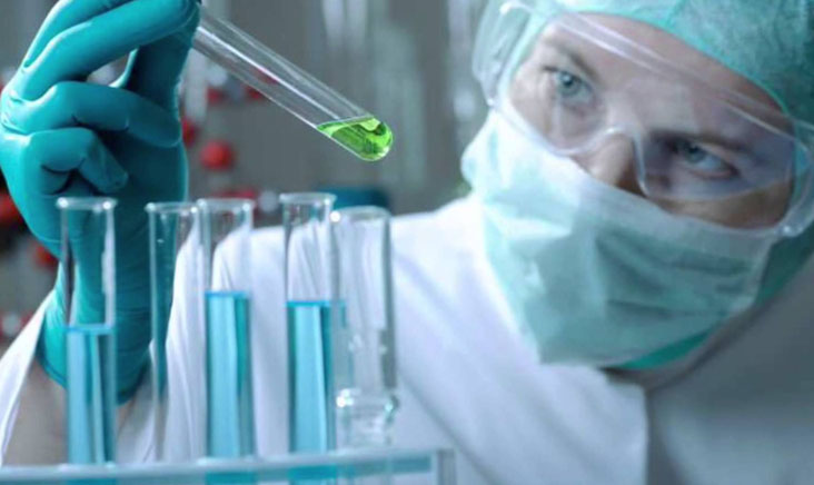 Women in hazad suit examining test tube with chemical inside