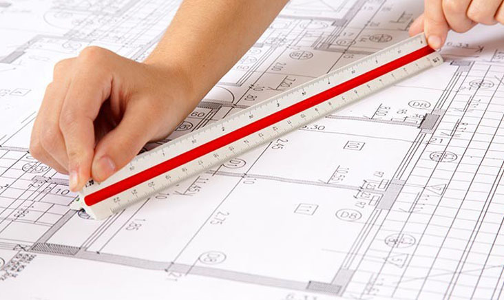 Hand holding ruler over plans for soundproofing party walls
